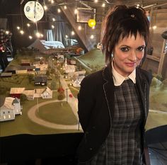 a woman standing in front of a model town with buildings and lights on the ceiling