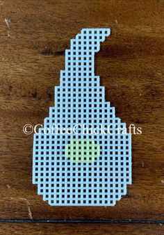 a cross stitch pattern with a green dot in the center on a wooden table top