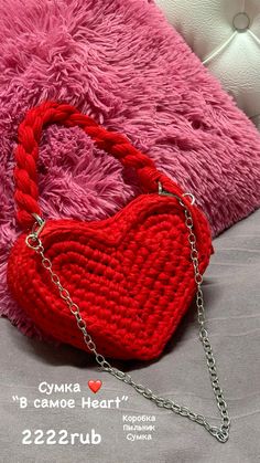 a red purse sitting on top of a bed next to a pink pillow and chain