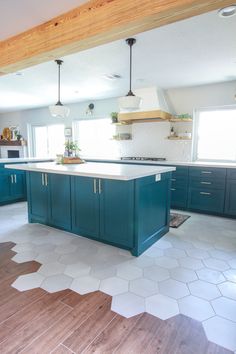 a large kitchen with blue cabinets and white tile flooring, along with wooden beams in the ceiling