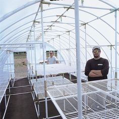 two men are standing in a greenhouse with white plastic structures and metal grates on the floor