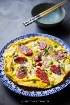 an omelet with pepperoni and green onions on a plate next to chopsticks