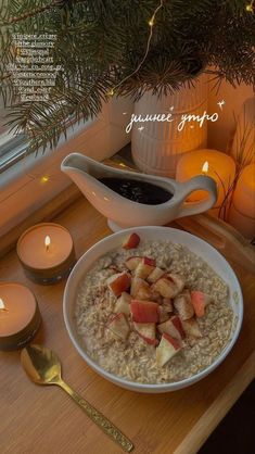 a bowl of oatmeal with apples and cinnamon sits on a table next to candles