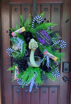 a wreath on the front door is decorated with green ferns and fake snake head decorations