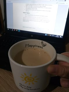 a person is holding a coffee cup in front of a laptop on a desk with the word happiness written on it