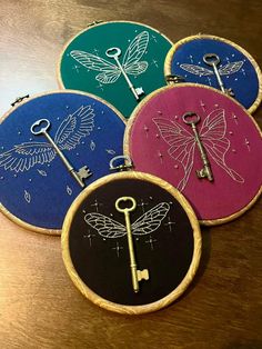 four embroidery hoops with key and dragon designs on them sitting on a wooden table