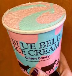 a hand holding up a blue bell of cream ice cream in it's cup