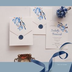 wedding stationery with blue flowers on white paper and ribbon next to an ornament