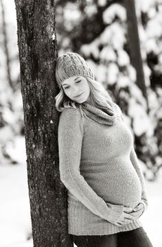 a pregnant woman leaning against a tree with her hands on her stomach in black and white