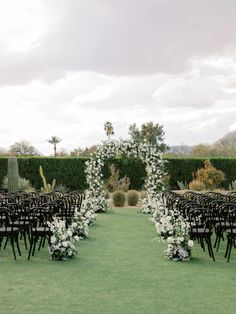 an outdoor ceremony setup with black chairs and white flowers on the aisle, surrounded by greenery