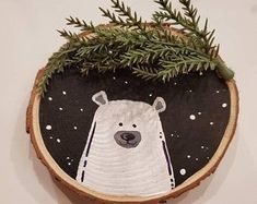 a wooden slice with a white bear on it and pine branches in the center, hanging on a wall