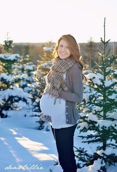 a pregnant woman standing in the snow with her hands on her belly and smiling at the camera