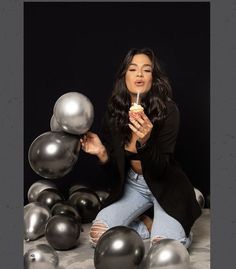 a woman sitting on the ground surrounded by silver balloons and holding a candle in her hand