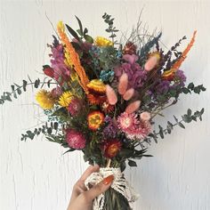 a person holding a bouquet of flowers in front of a white wall with greenery