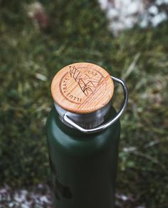 a green water bottle with a wooden lid sitting on the ground next to some grass