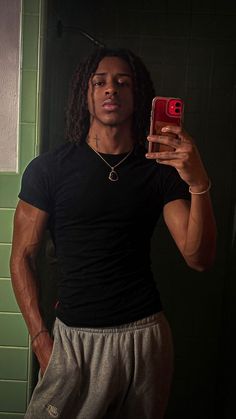 a man taking a selfie with his cell phone in a bathroom stall, while wearing sweatpants