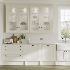 a white kitchen with lots of glass cabinets and counter top space in front of a window