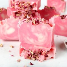 pink soap bars with flowers on them sitting next to a bowl of dried rose petals