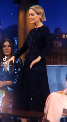 a woman in a black dress is standing on a stage with her hands behind her back