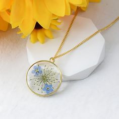 Our gorgeous Crystal Epoxy Resin Floral Neckless will add a touch of elegance to your jewelry collection. This one-of-a-kind creation, which has actual flowers preserved in crystal-clear resin, beautifully depicts the beauty of nature. The pendant is the ideal addition to any ensemble because of its vivid flower pattern, which adds a touch of elegance and uniqueness. Nature-Inspired Design: Every pendant is made by hand using actual flowers, guaranteeing a unique creation that honors the splendor of the natural world. Superior Quality: Constructed from premium epoxy resin, the pendant is lightweight and strong, making it comfortable to wear all day. Standard Chain Length: The pendant's 20-inch chain beautifully matches the pendant's style. Customizable Options: To make your pendant unique, Nature-inspired Resin Jewelry, Elegant Glass Flower Necklaces, Elegant Flower-shaped Glass Necklaces, Elegant Flower Shaped Glass Necklaces, Nature-inspired Birth Flower Resin Jewelry, Elegant Glass Flower Necklace, Nature-inspired Resin Birth Flower Jewelry, Elegant White Pressed Flower Necklace, Botanical Style Gold Resin Jewelry