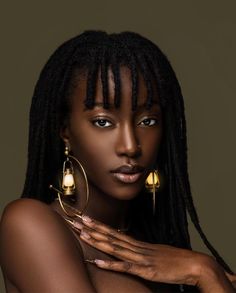 a woman with dreadlocks and gold earrings on her chest, posing for the camera