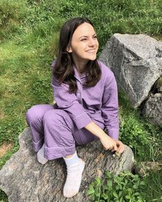 a woman sitting on top of a rock next to green grass and rocks in the background