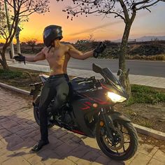 a shirtless man sitting on top of a motor bike next to a tree at sunset