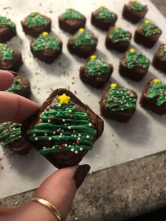 a hand holding a piece of brownie with green frosting and christmas trees on it