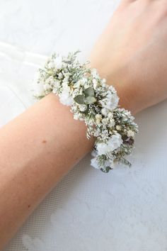 a woman's arm with white flowers and greenery attached to it, on top of a table