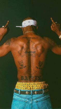 the back of a man with tattoos on his chest and hands up in the air