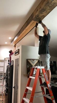 two men are working on a beam in a room that is being remodeled with ladders