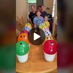 a group of people standing around a wooden table with bowling balls on it and smiling