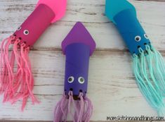 three colorful paper tubes with eyes and hair on them sitting on top of a wooden table