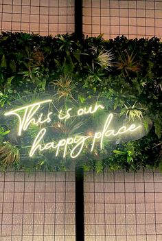 this is our happy place neon sign in front of a wall with plants on it