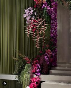 an arrangement of flowers on the side of a staircase in front of a green curtain