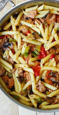 pasta with meat and vegetables in a pan on a wooden table next to utensils