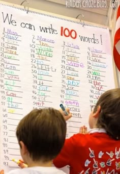 two children writing on a bulletin board with the words we can write 100 words in front of them