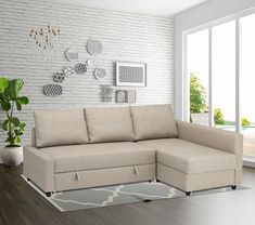 a living room with white brick walls and wood flooring, a beige sectional sofa sits in front of a large window