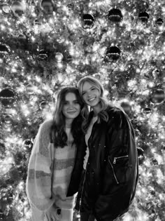 two women standing next to each other in front of a christmas tree with lights on it