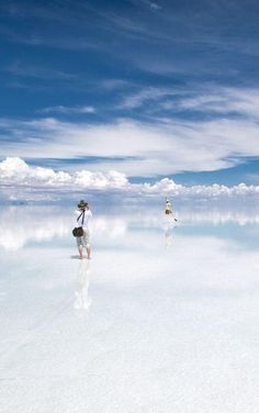 two people standing in the middle of a salt flat with blue skies and white clouds