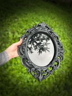 a person holding up a mirror with a tree in the center and grass behind it