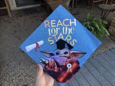 someone is holding up a graduation cap with an image of baby yoda and the words reach for the stars on it