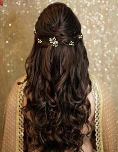 the back of a woman's head with long curly hair and gold accessories on it