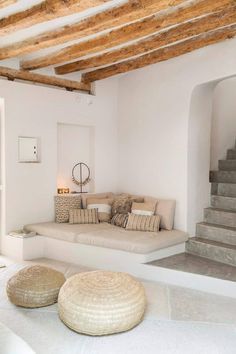 a living room filled with white furniture and wooden beams on top of the ceiling next to a set of stairs