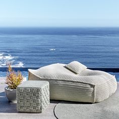 an outdoor seating area overlooking the ocean with pillows and rugs on concrete flooring