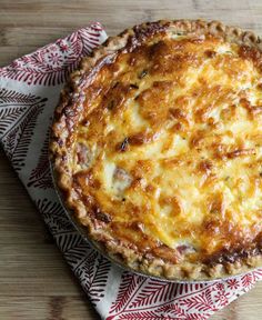 a quiche with cheese on top sitting on a napkin next to a fork and knife