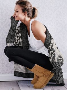 a woman is sitting on the floor with her feet up and wearing black pants, a white tank top and brown boots