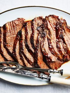 a white plate topped with sliced up steak next to a knife and fork on top of a table