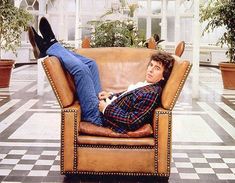 a man laying on top of a brown chair in a room with black and white checkered flooring