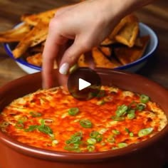 a person dipping some olives into a bowl of dip with tortilla chips in the background